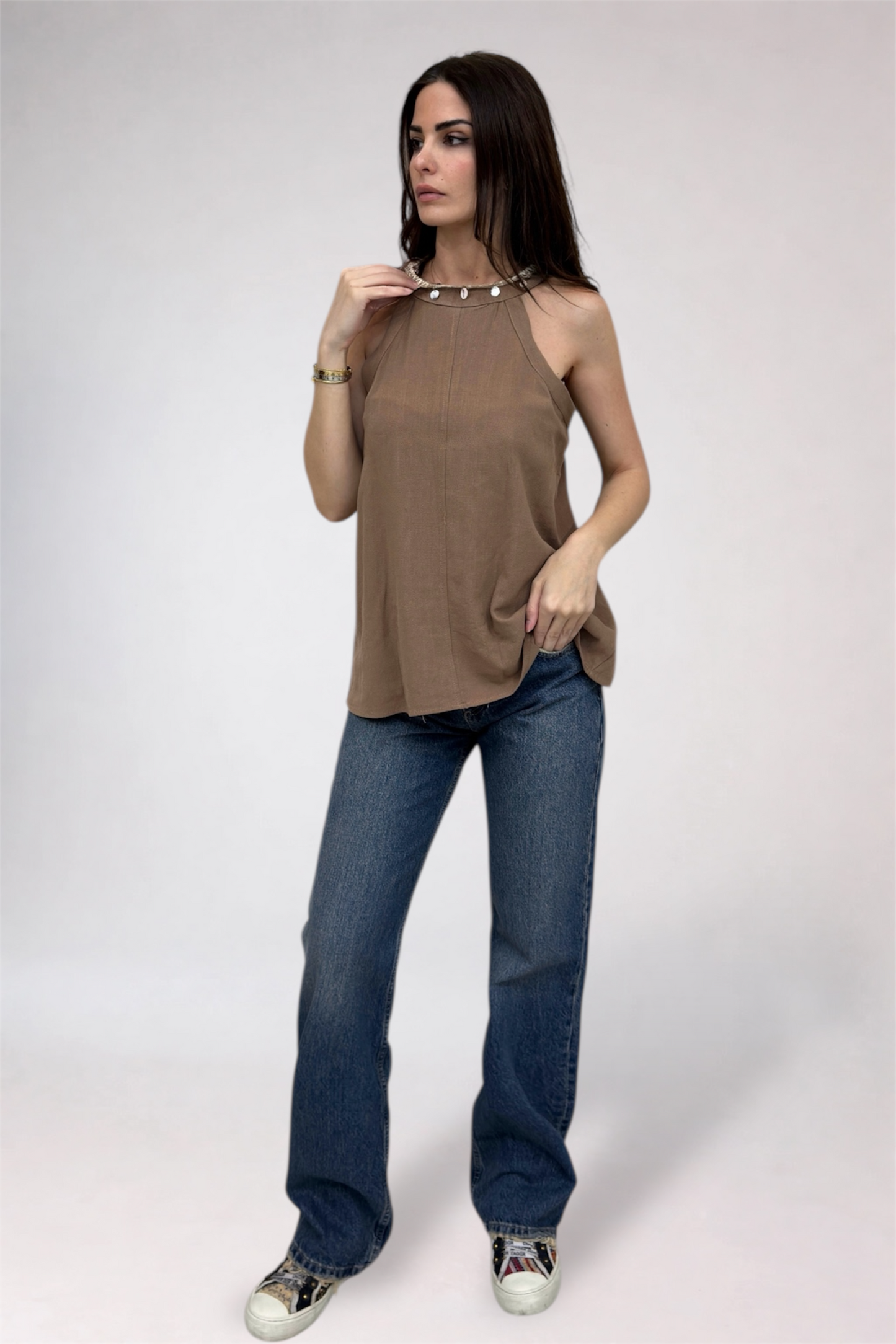 Woman wearing a brown sleeveless top and blue jeans on a white background