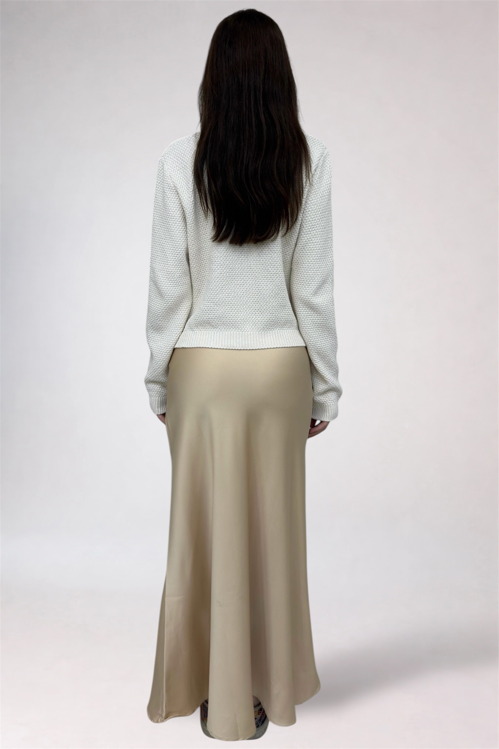 Person wearing a white sweater and beige skirt on a plain background