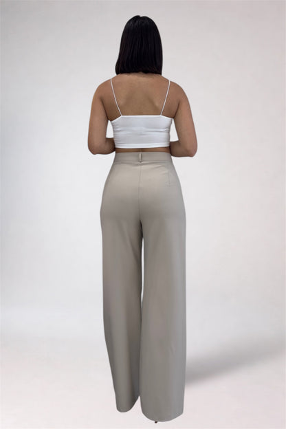 Woman wearing a white top and beige high-waisted pants on a plain background