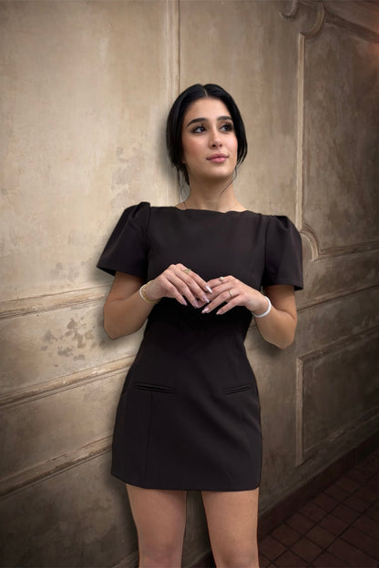 Woman wearing a black dress against a textured wall.