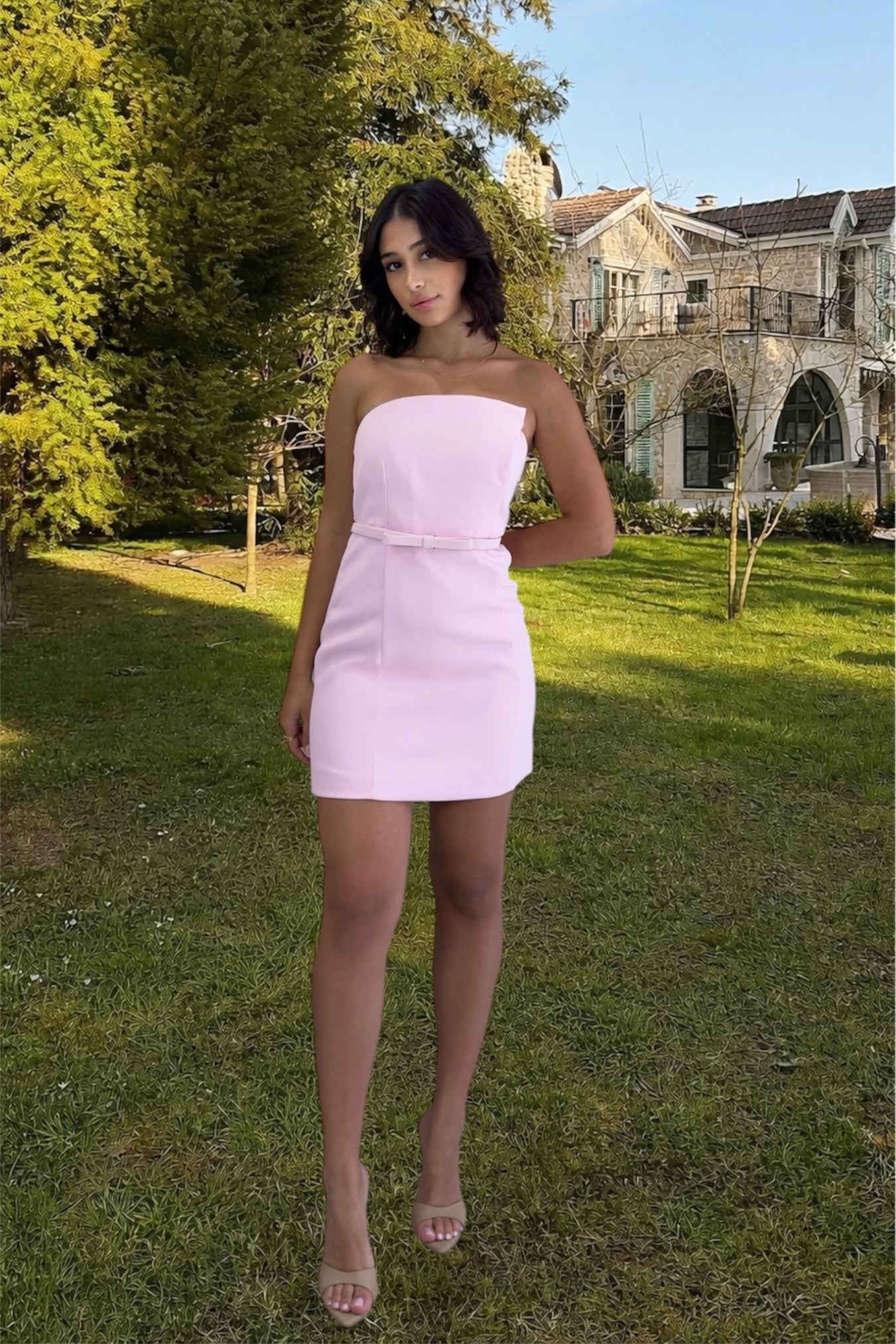 Woman in a pink dress standing in a garden with a house in the background