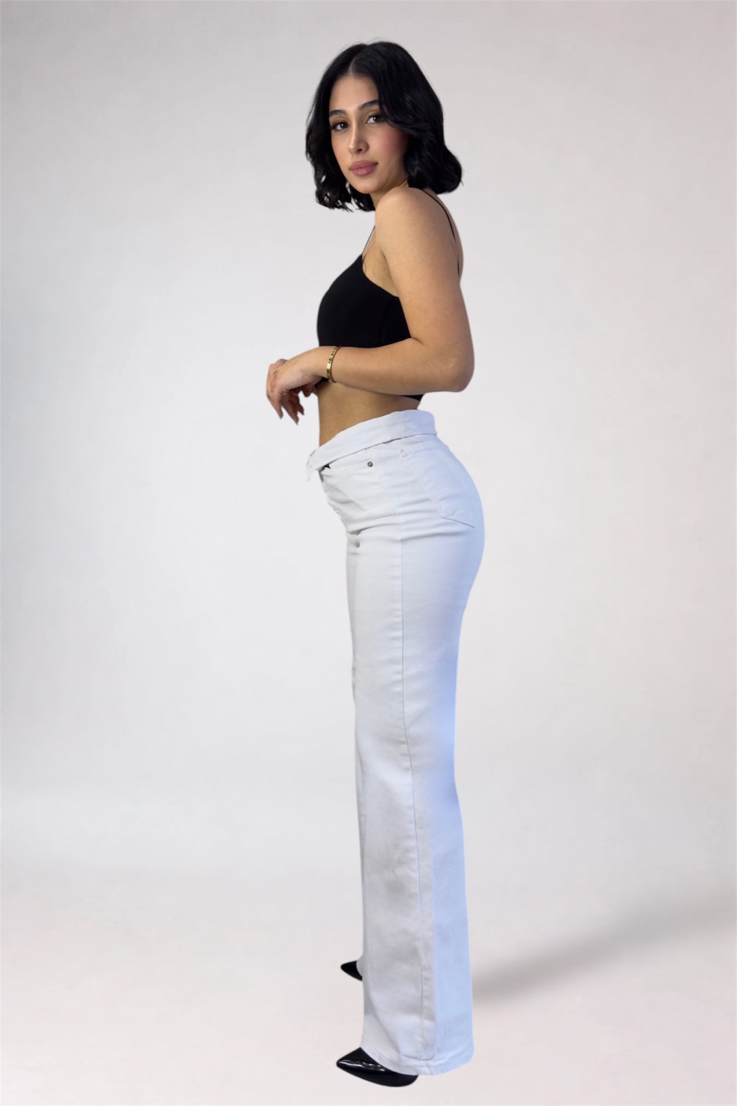 Woman wearing white jeans and a black top on a plain background