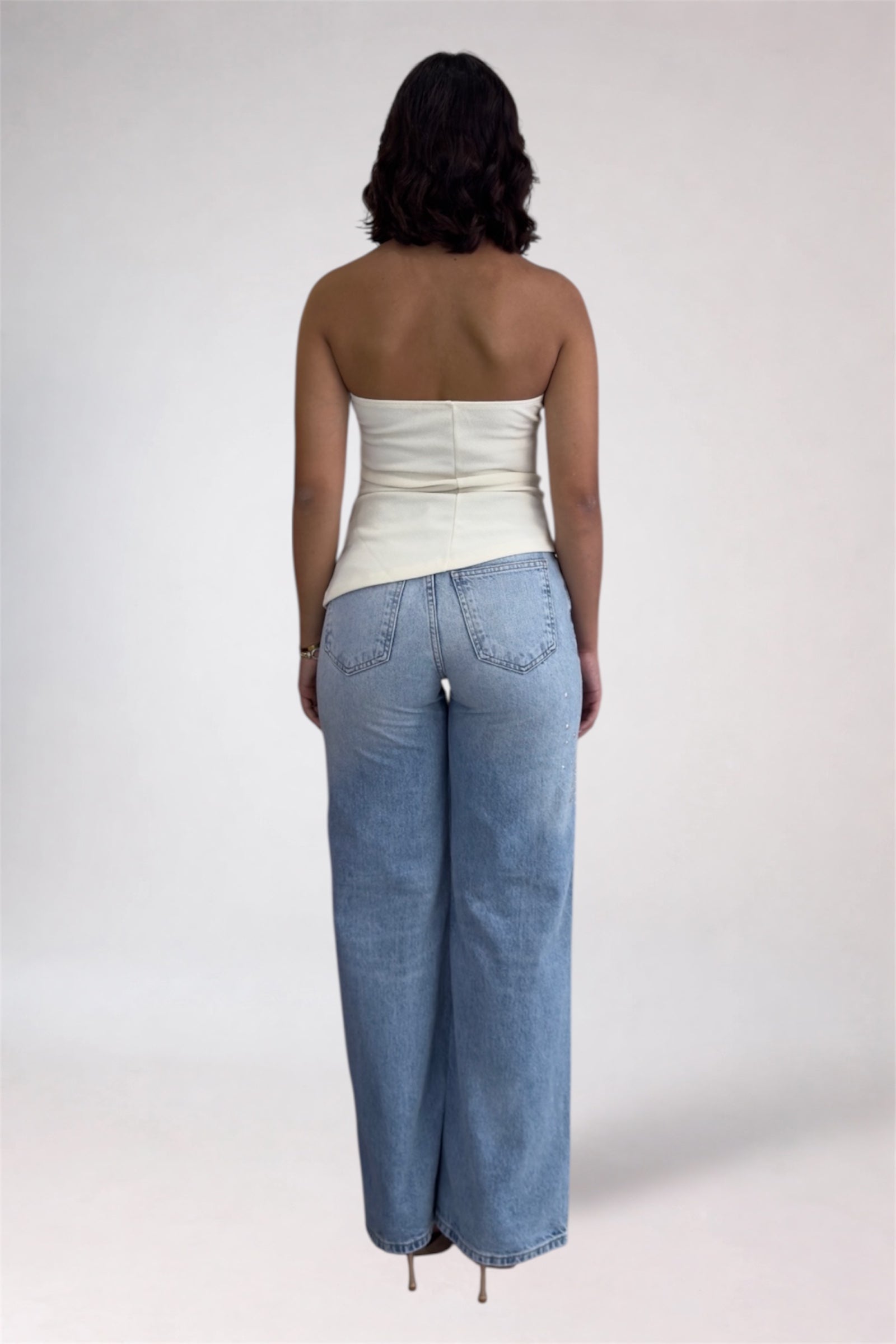 Person wearing a strapless top and light blue jeans on a plain background
