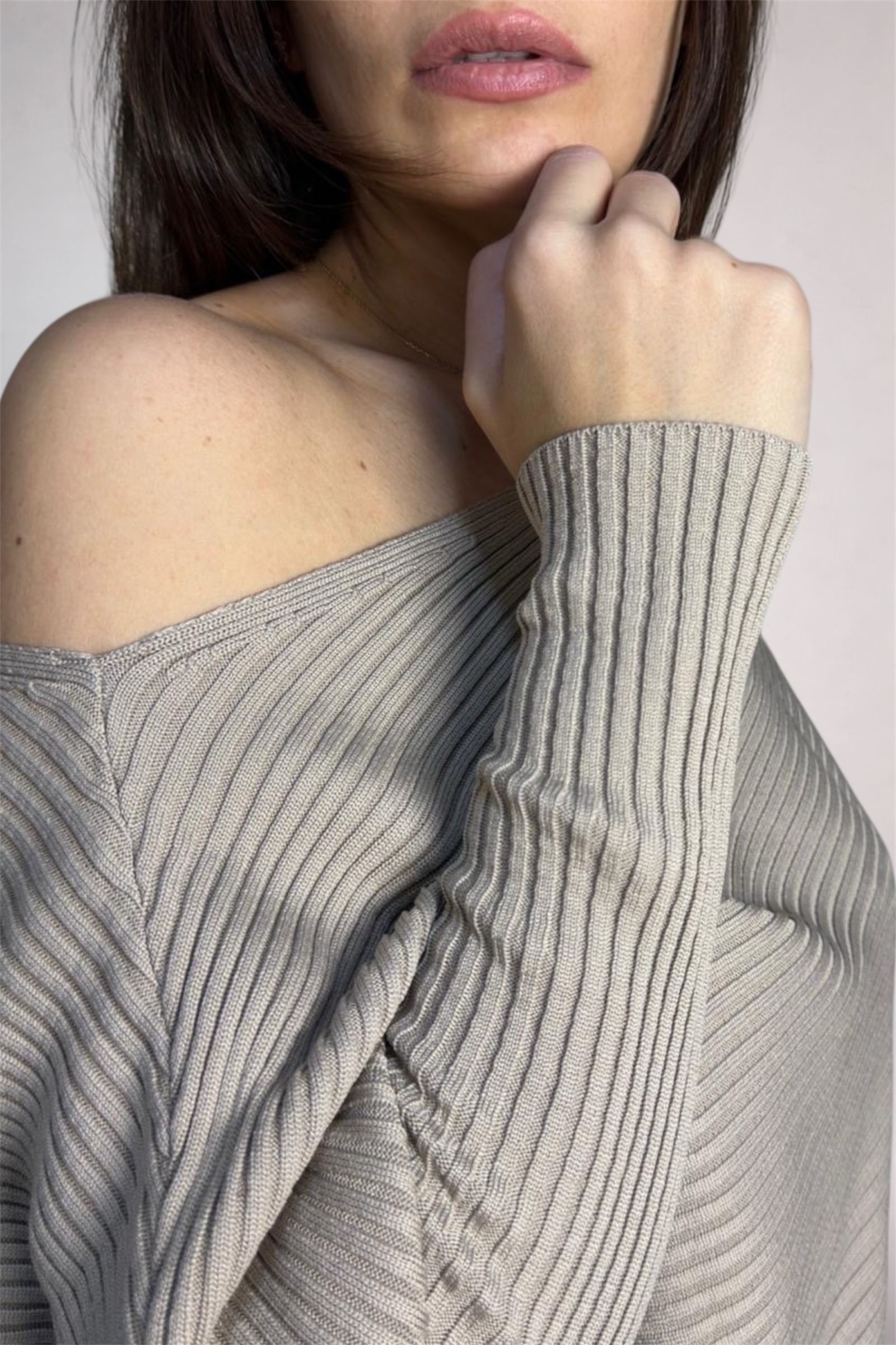 Close-up of a person wearing a gray ribbed sweater with a plain background