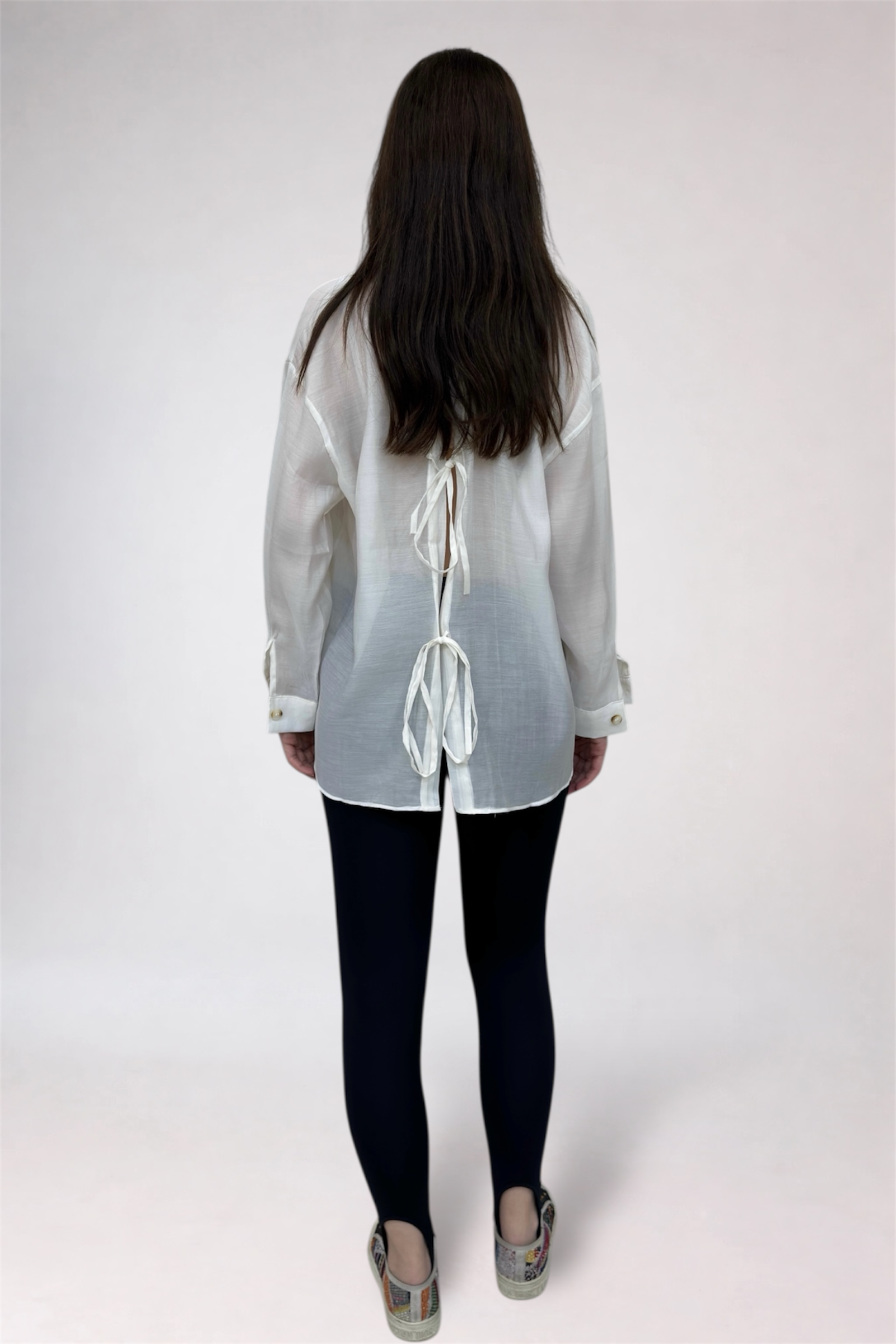 Person wearing a sheer white top with black leggings on a white background