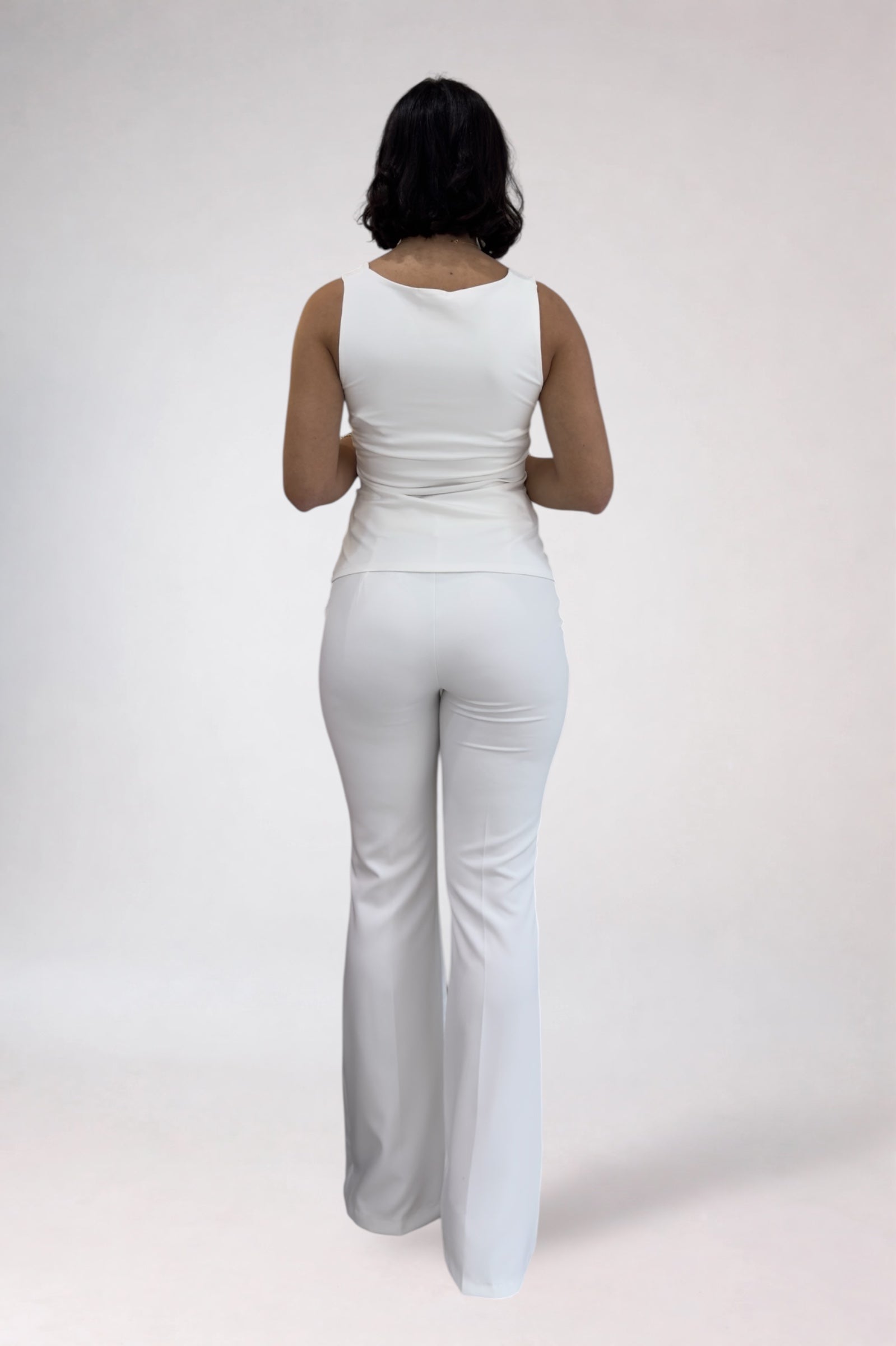 Person wearing a white sleeveless top and pants set on a plain background