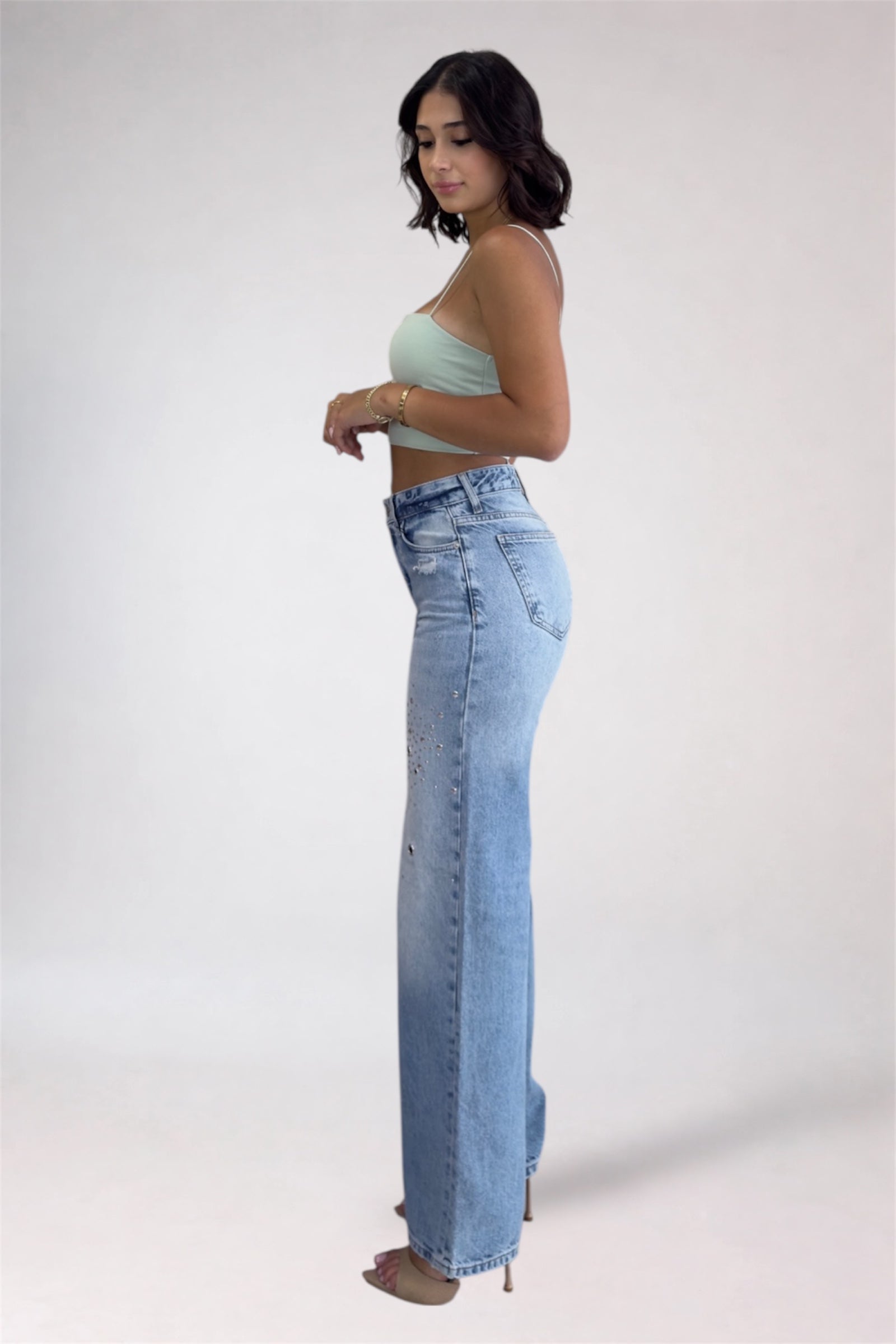Woman wearing light blue jeans and a green top on a white background