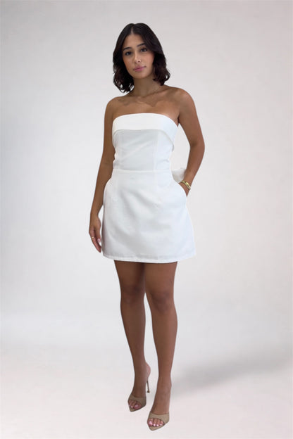 Woman wearing a white strapless dress against a plain background