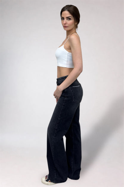 Woman wearing a white crop top and black wide-leg jeans on a plain background