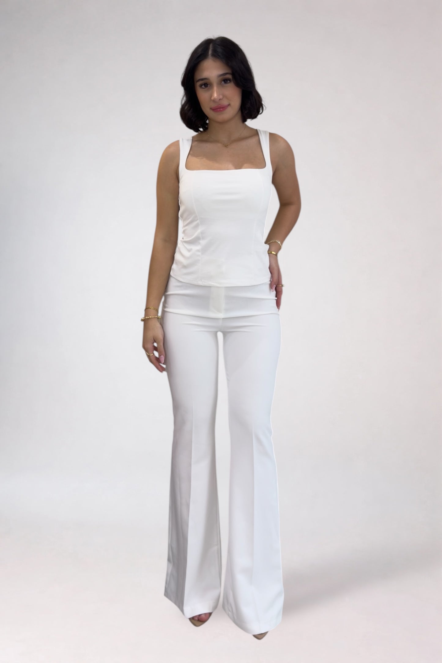 Woman wearing a white sleeveless top and white pants on a plain background