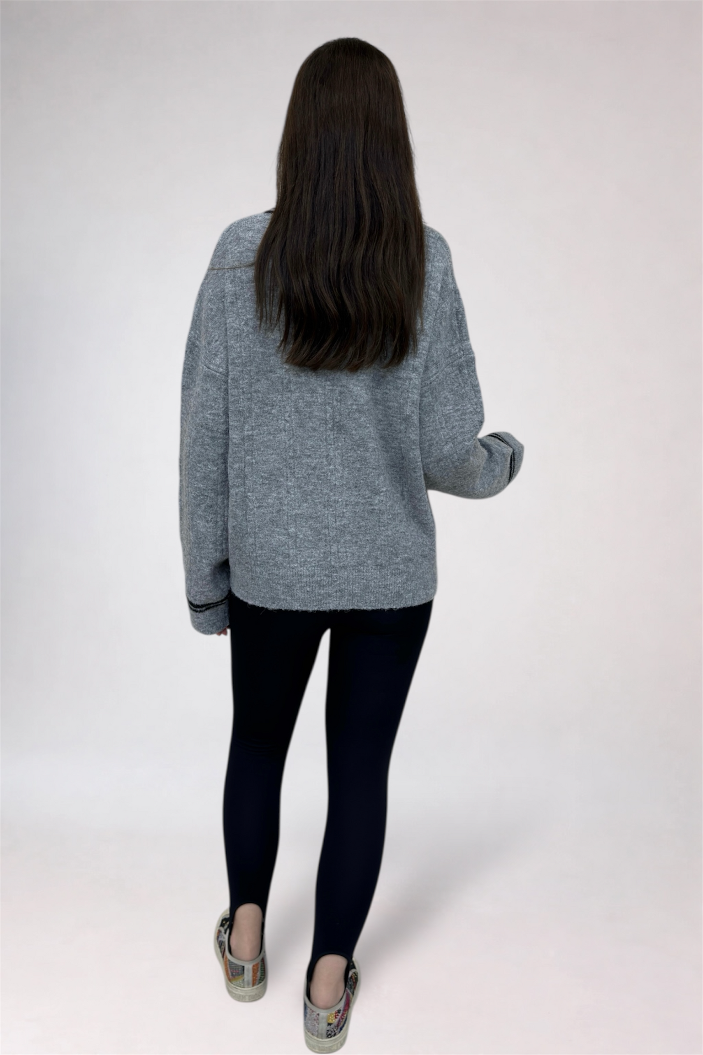 Person wearing a gray sweater and black pants on a white background