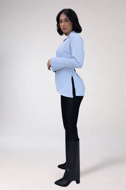 Woman wearing a light blue blazer, black pants, and black boots on a white background