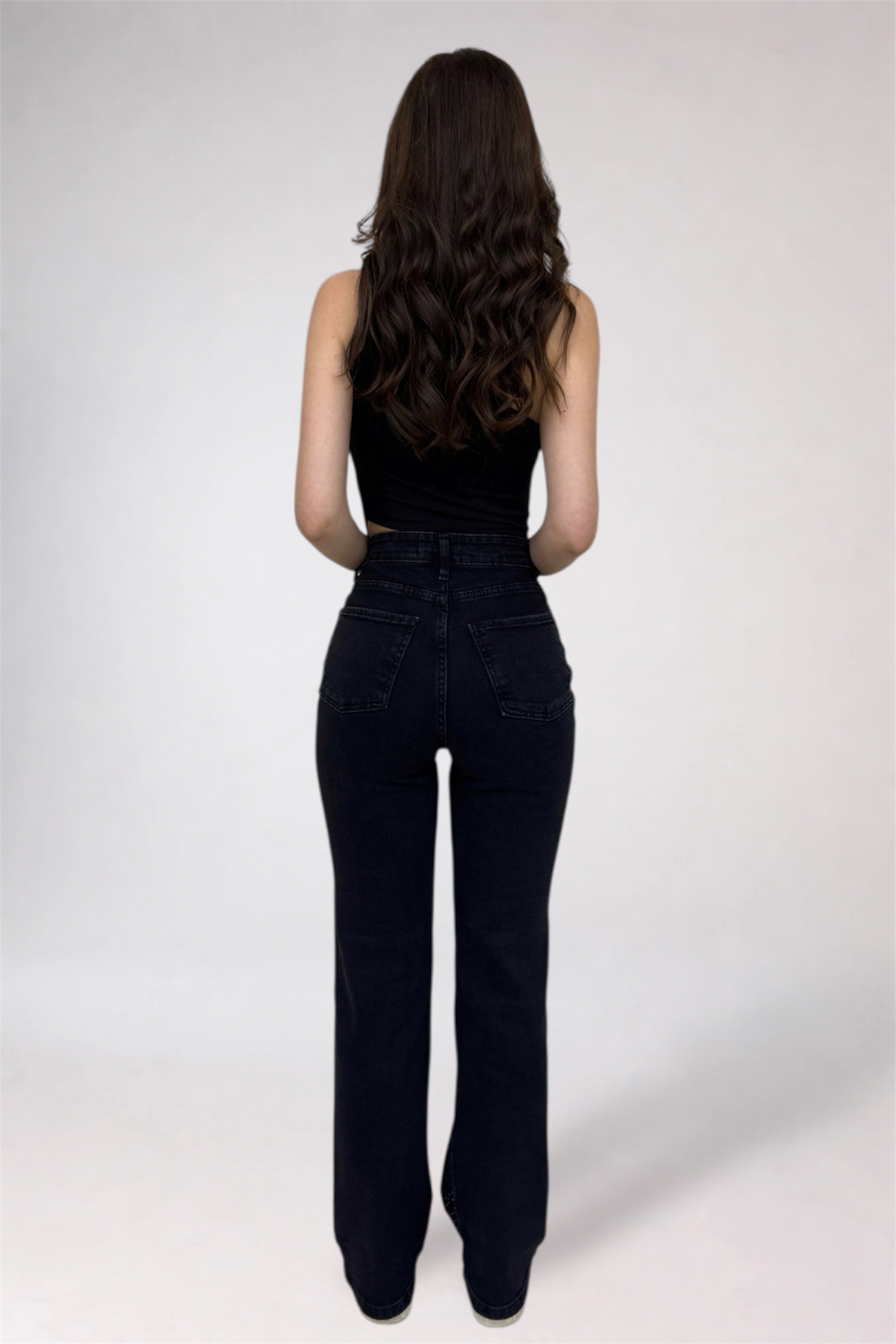 Person wearing black high-waisted jeans and a black top on a white background