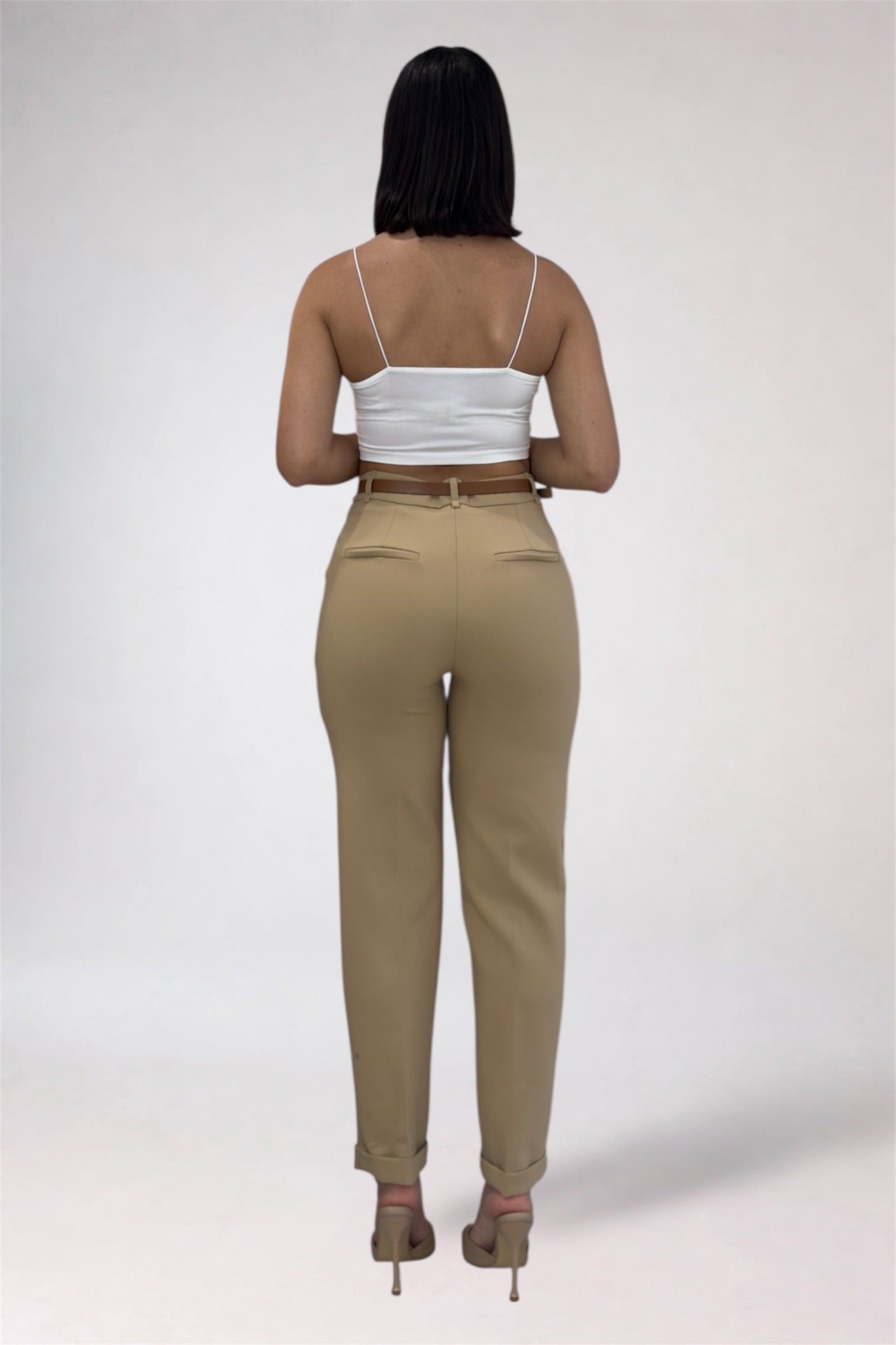 Woman wearing beige pants and a white top on a plain background