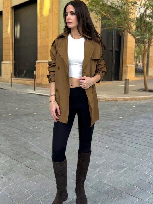 Woman wearing a brown trench coat, white top, black pants, and brown knee-high boots on a street.