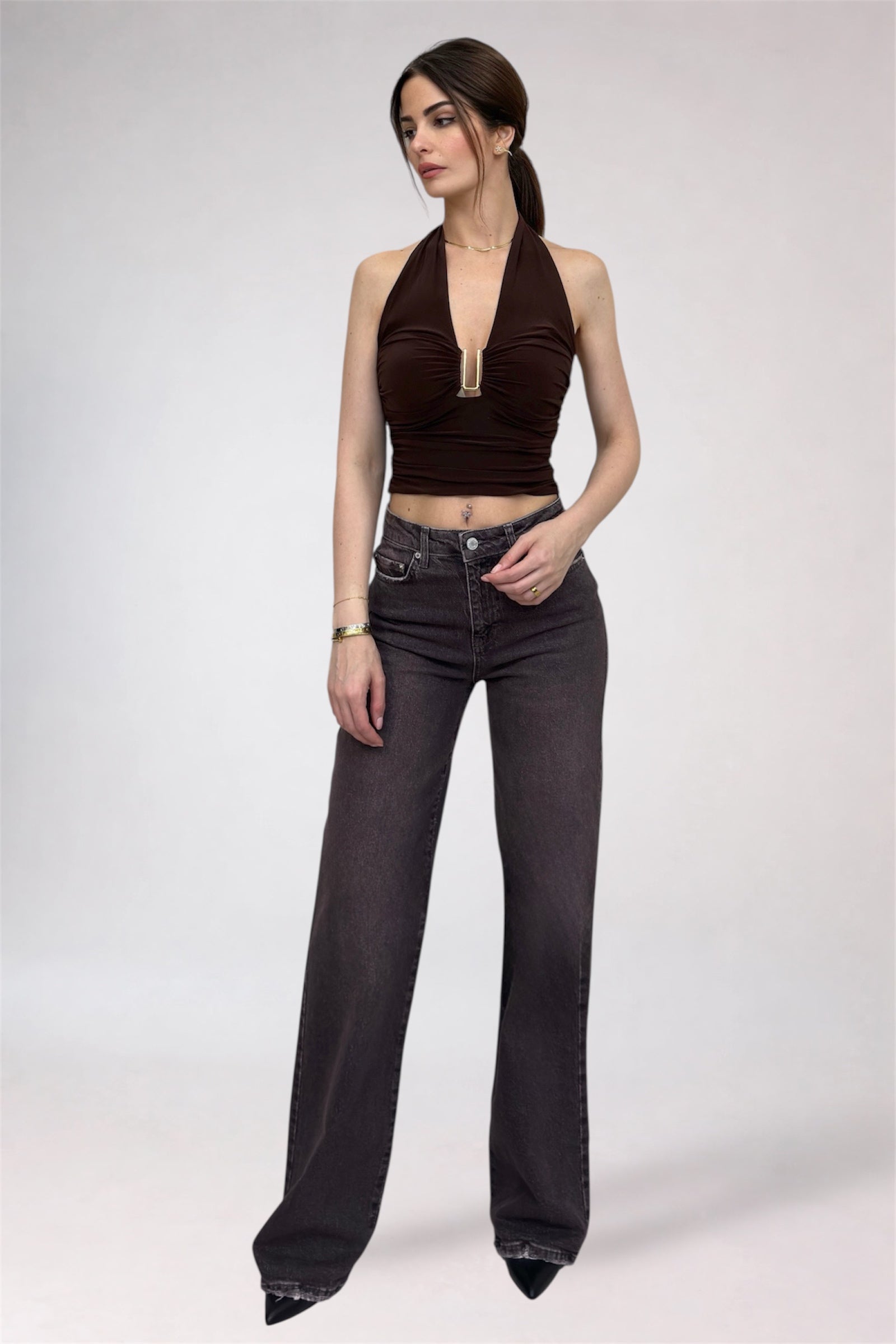 Woman wearing a brown halter top and dark jeans on a white background