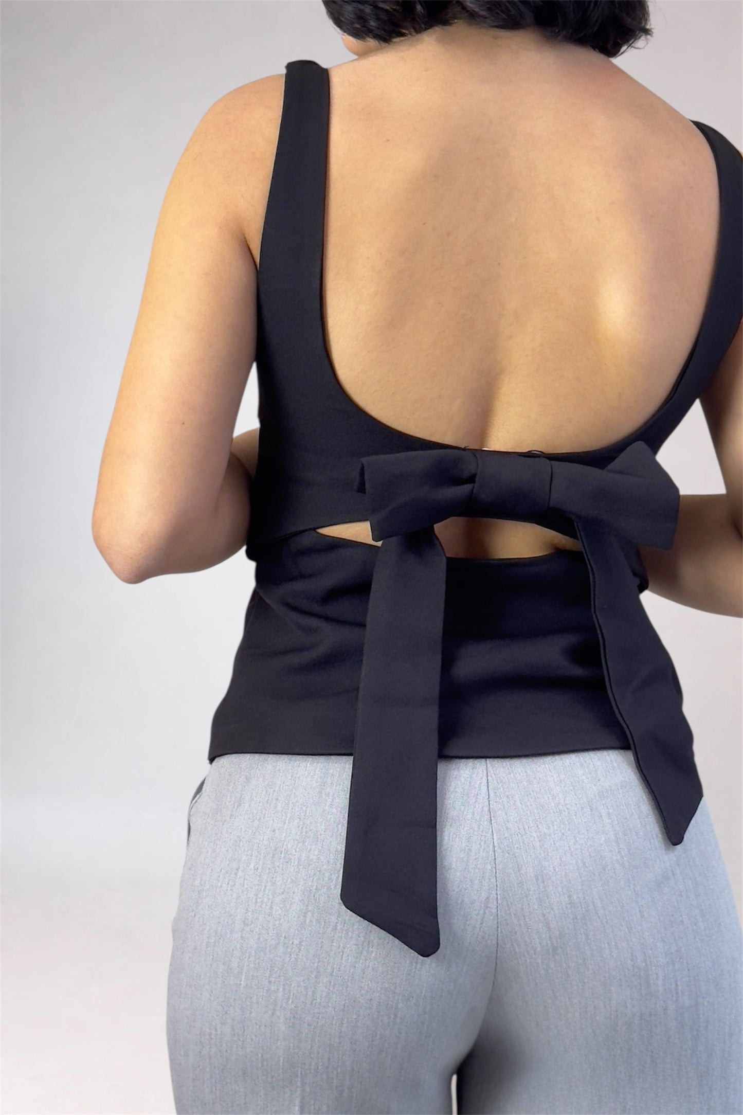 Black open-back top with a bow detail on a plain background