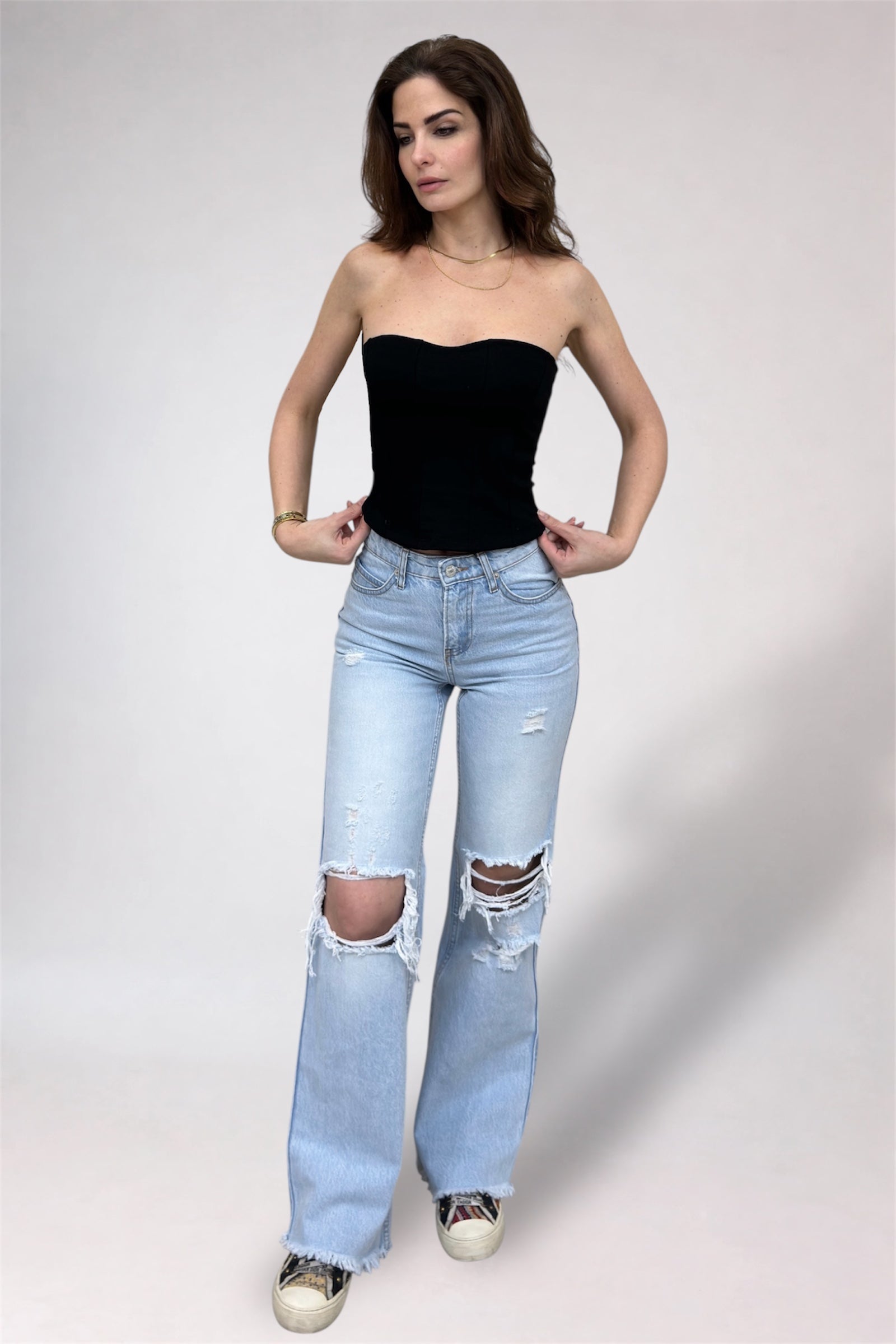 Woman wearing a black strapless top and light blue ripped jeans on a white background