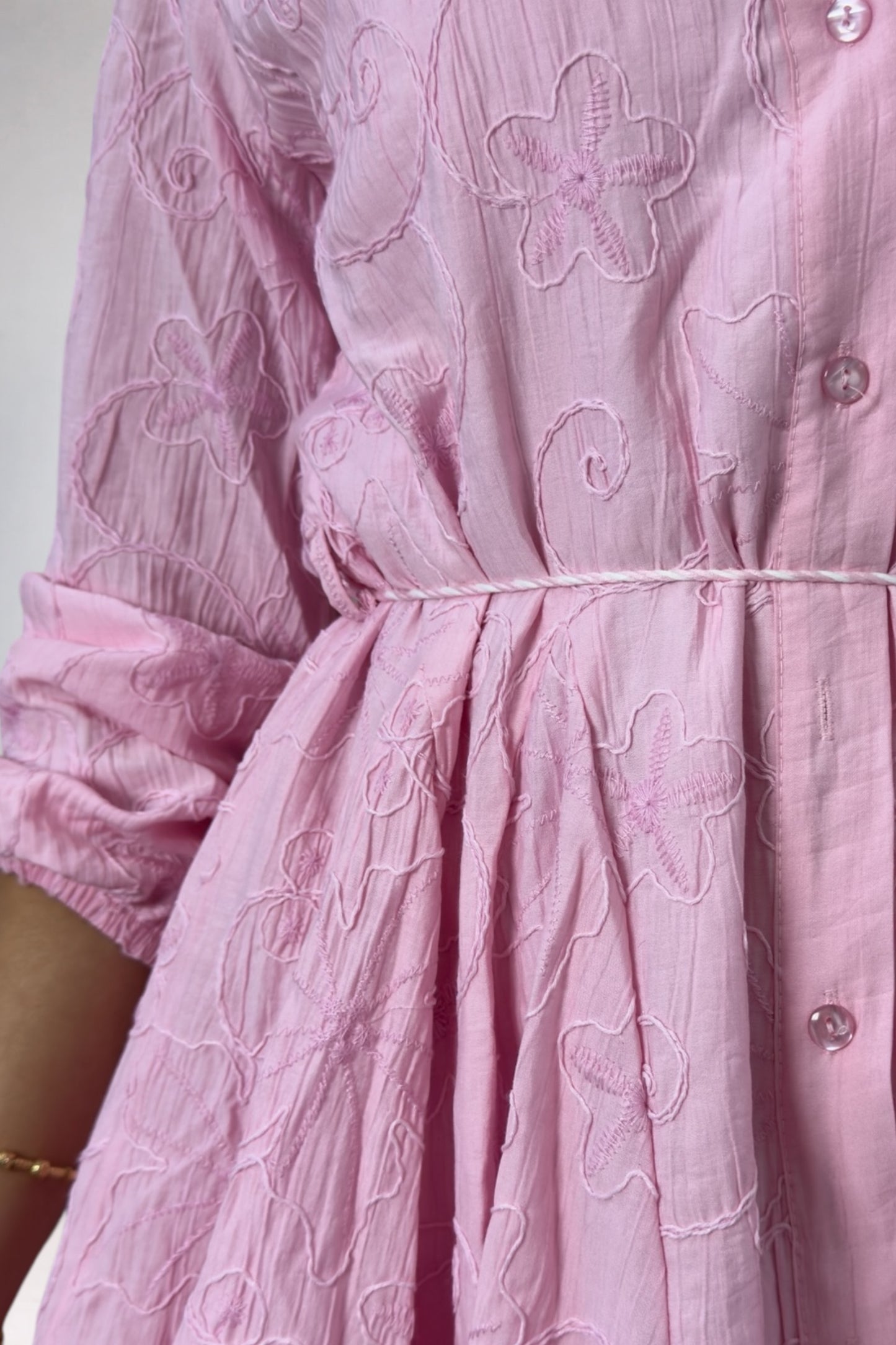 Close-up of a pink dress with floral embroidery on a plain background