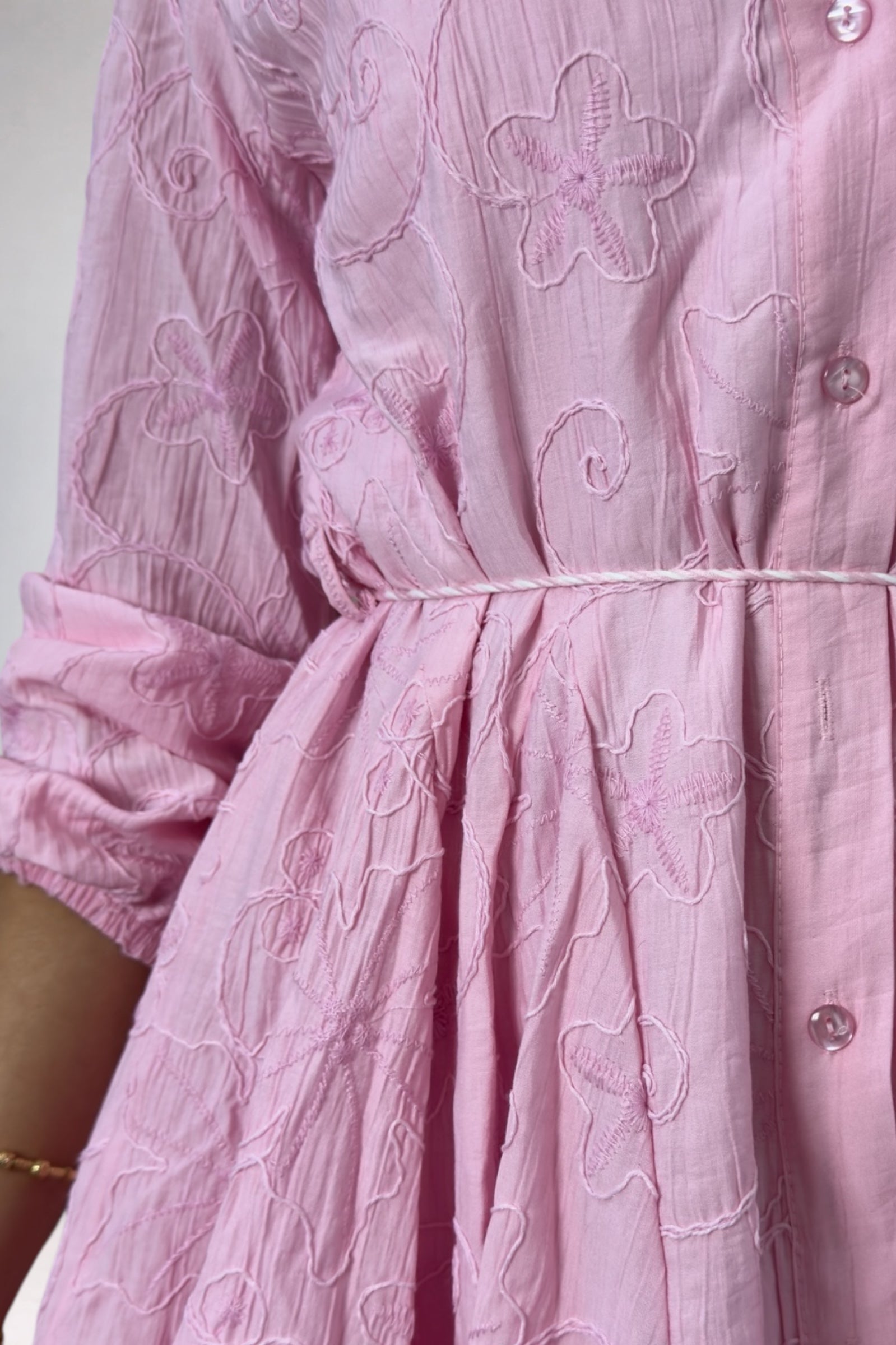 Close-up of a pink dress with floral embroidery on a plain background