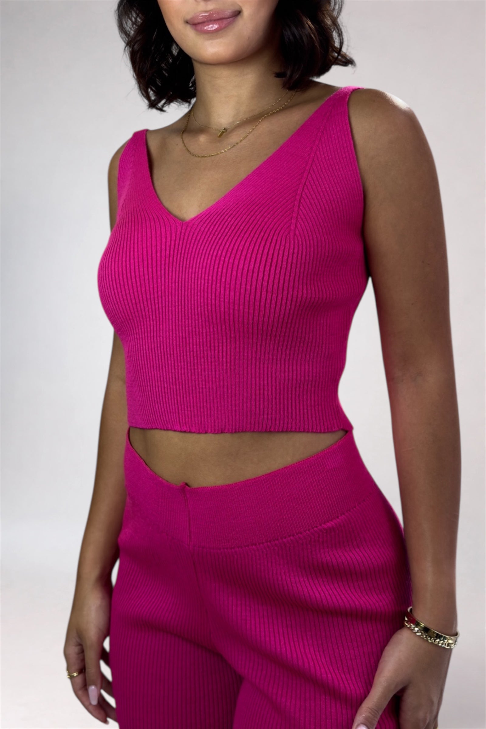 Woman wearing a bright pink sleeveless top and skirt set against a plain background
