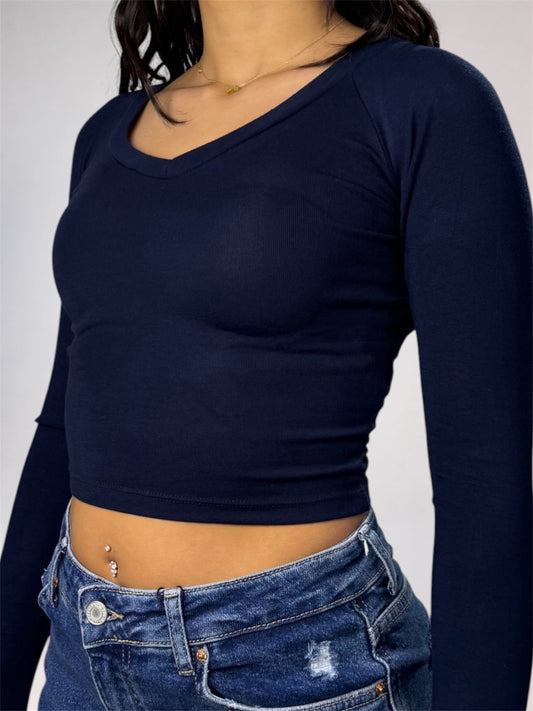 A woman wearing a dark navy blue long-sleeve crop top with a wide scoop neckline, paired with blue jeans.