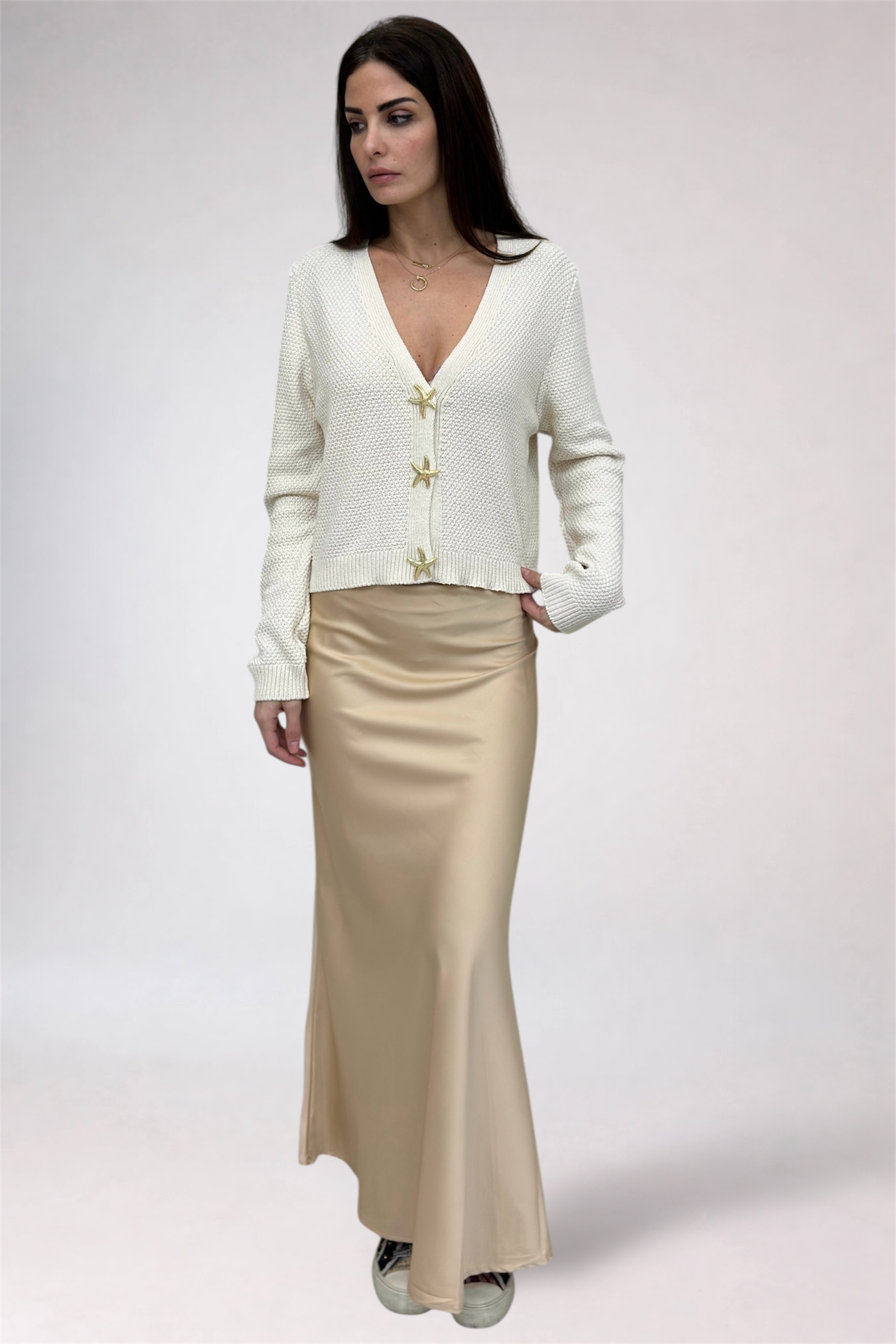 Woman wearing a white cardigan and beige skirt on a plain background