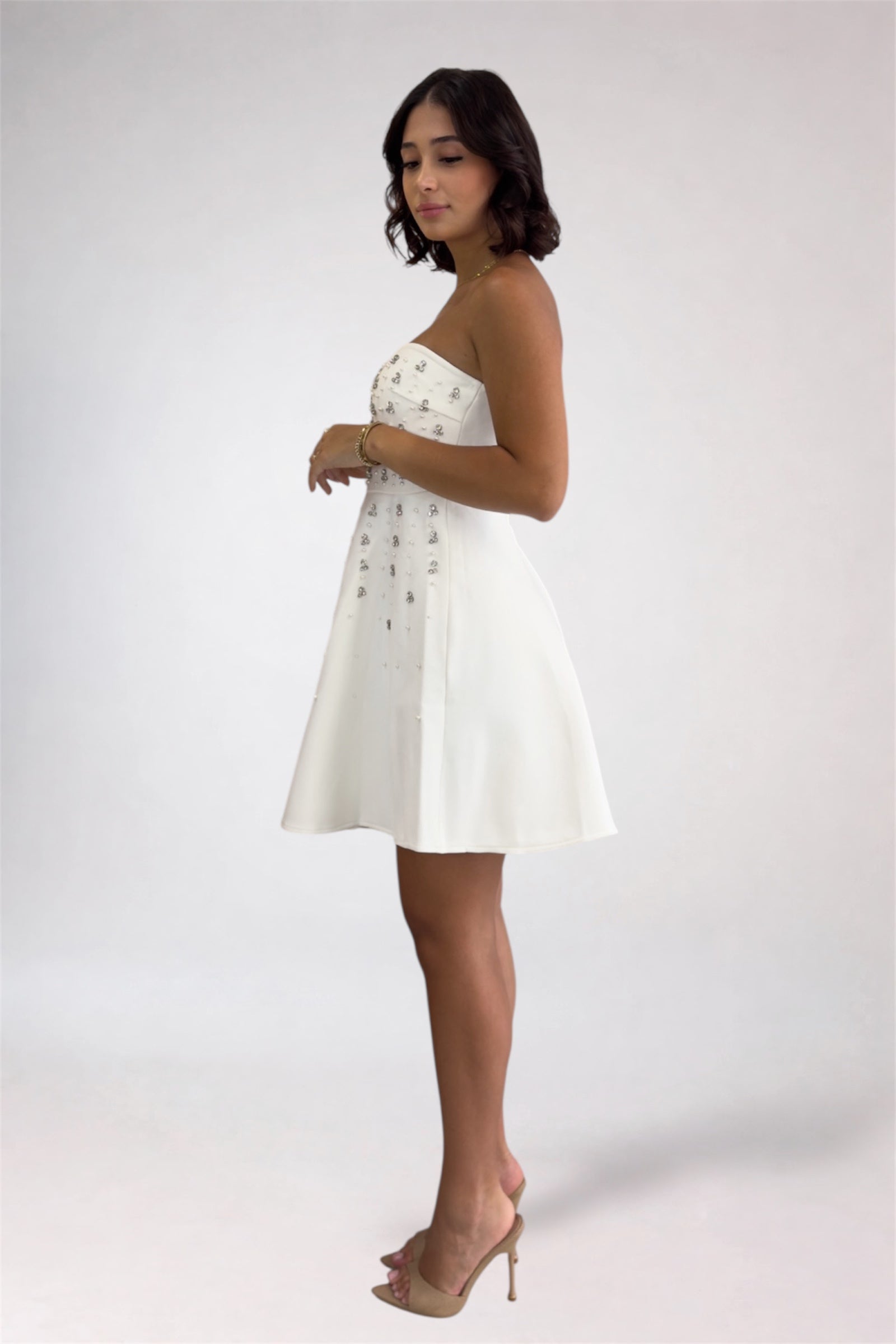 Woman wearing a white strapless dress with buttons on a plain background