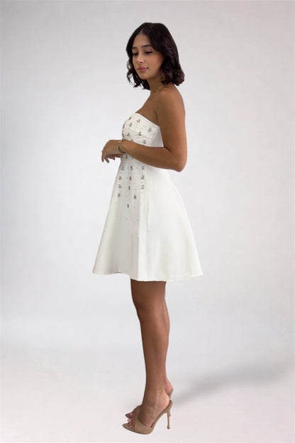 Woman wearing a white strapless dress with buttons on a plain background