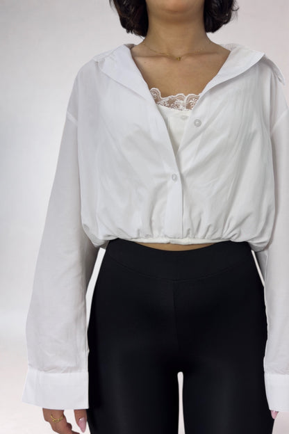 Person wearing a white blouse with lace details and black pants on a plain background