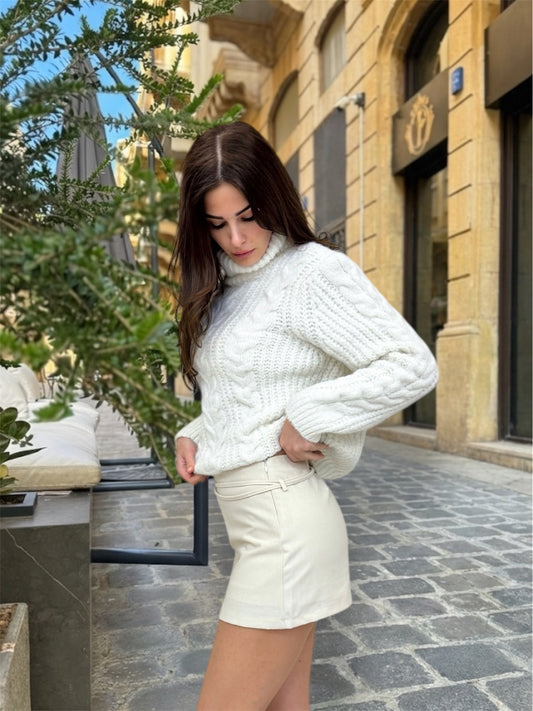 Woman wearing a white cable knit sweater and cream shorts in an outdoor setting.