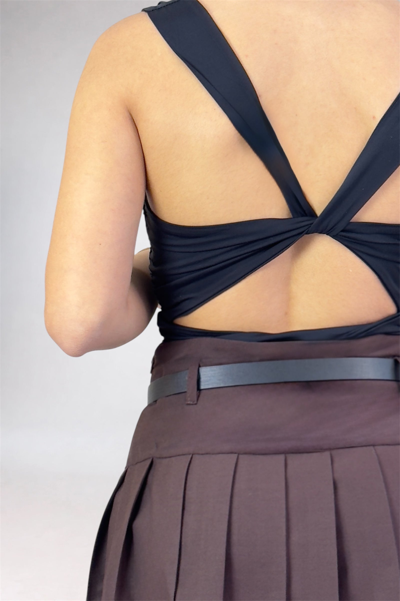 Black top with open back and pleated skirt on a plain background