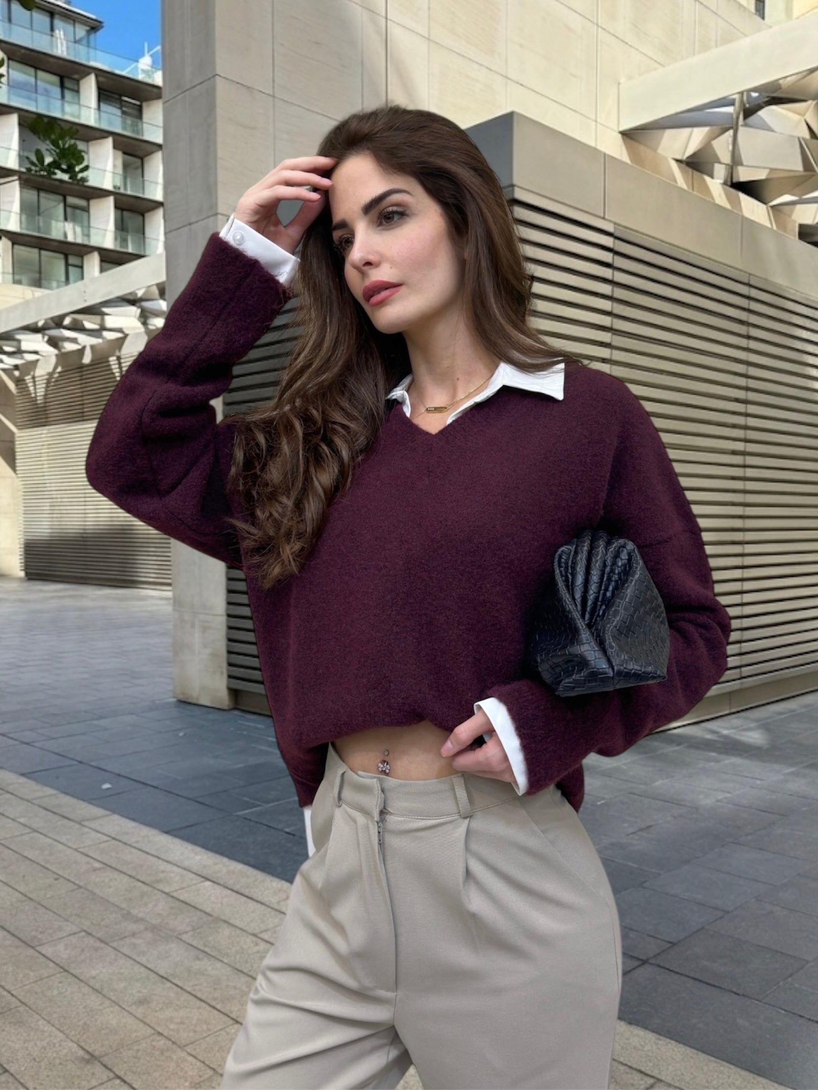 Woman in a burgundy sweater and beige pants standing in an urban setting