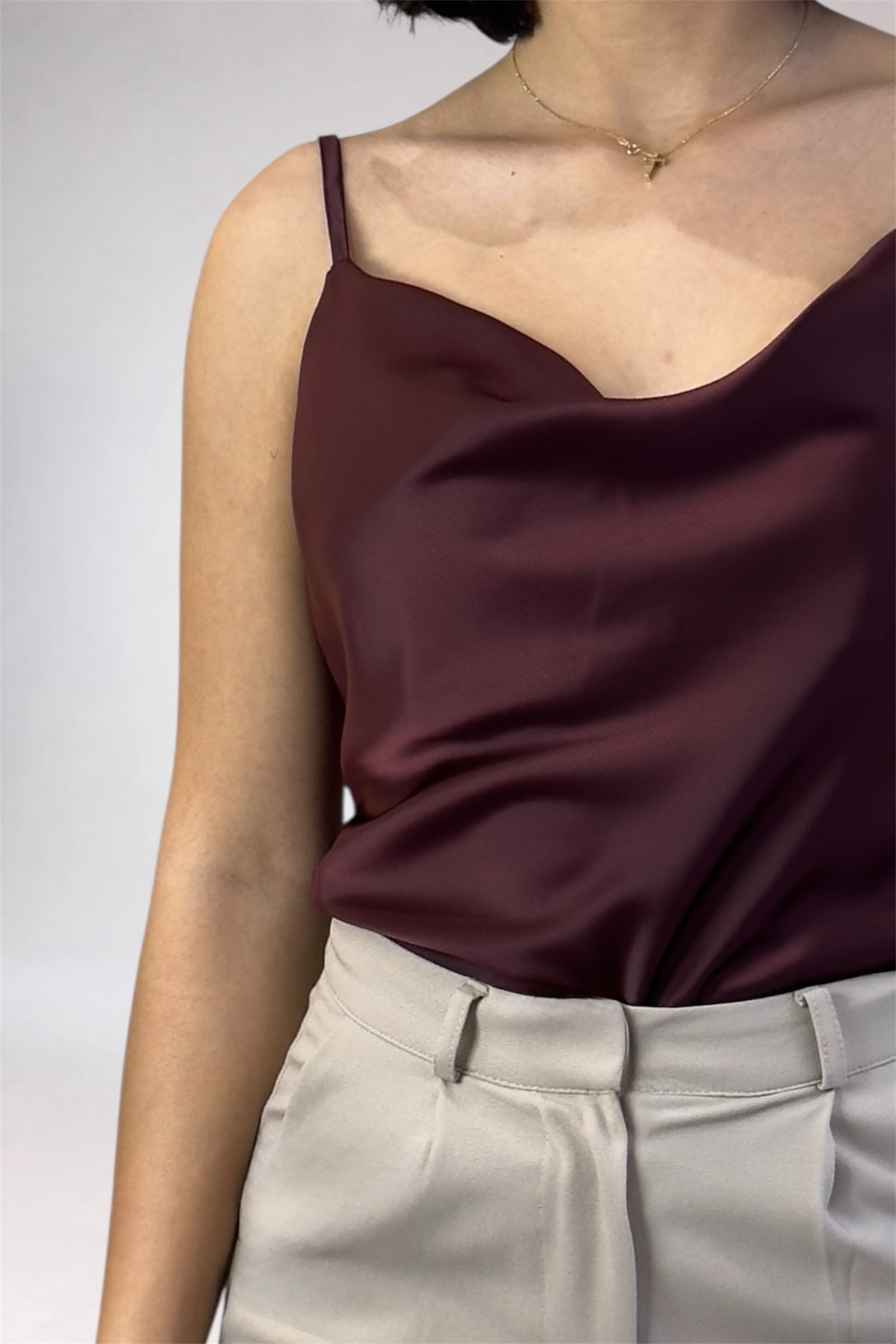 Person wearing a burgundy satin top and beige pants against a neutral background