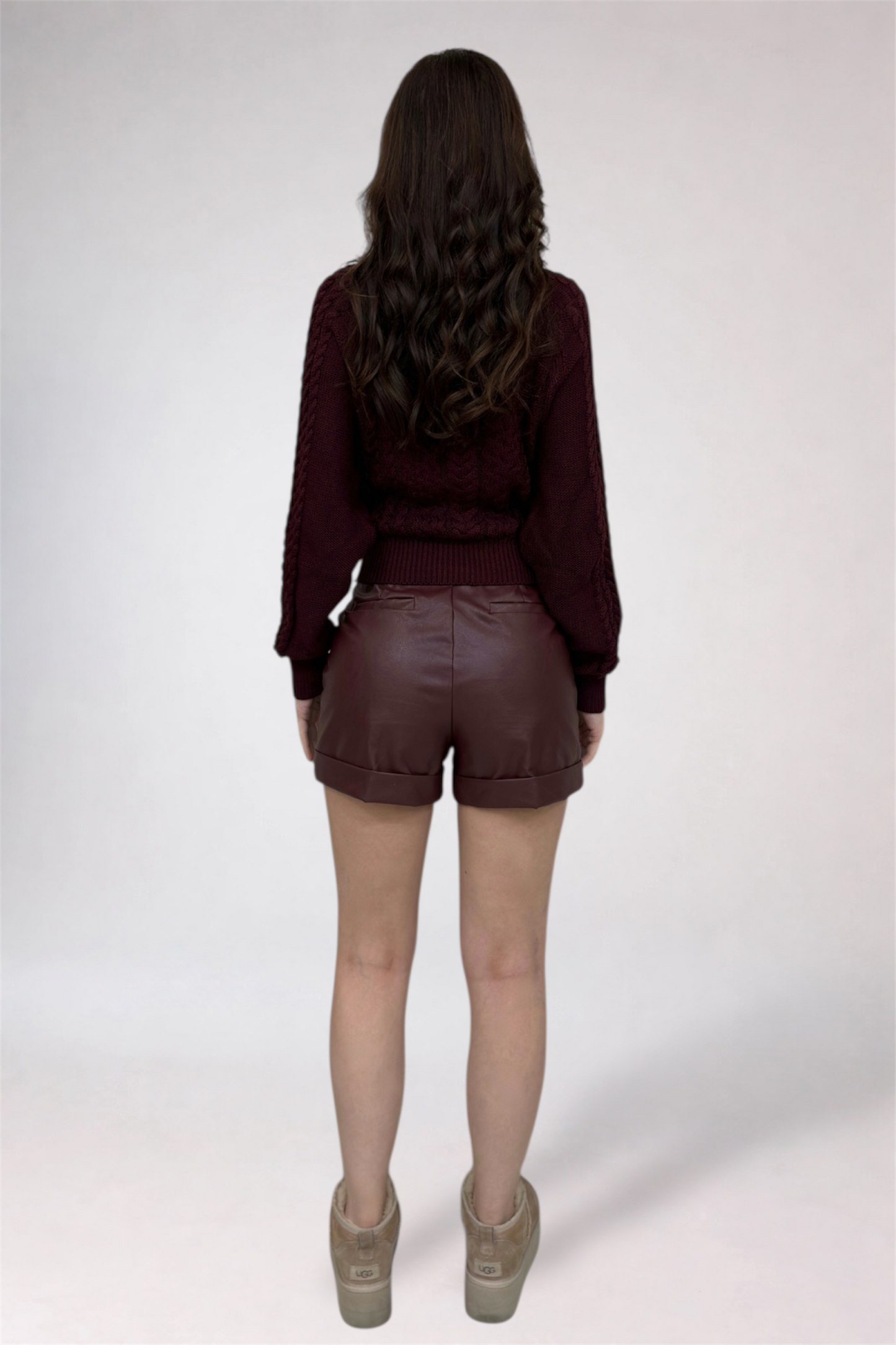 Person wearing a maroon sweater and brown leather shorts on a white background