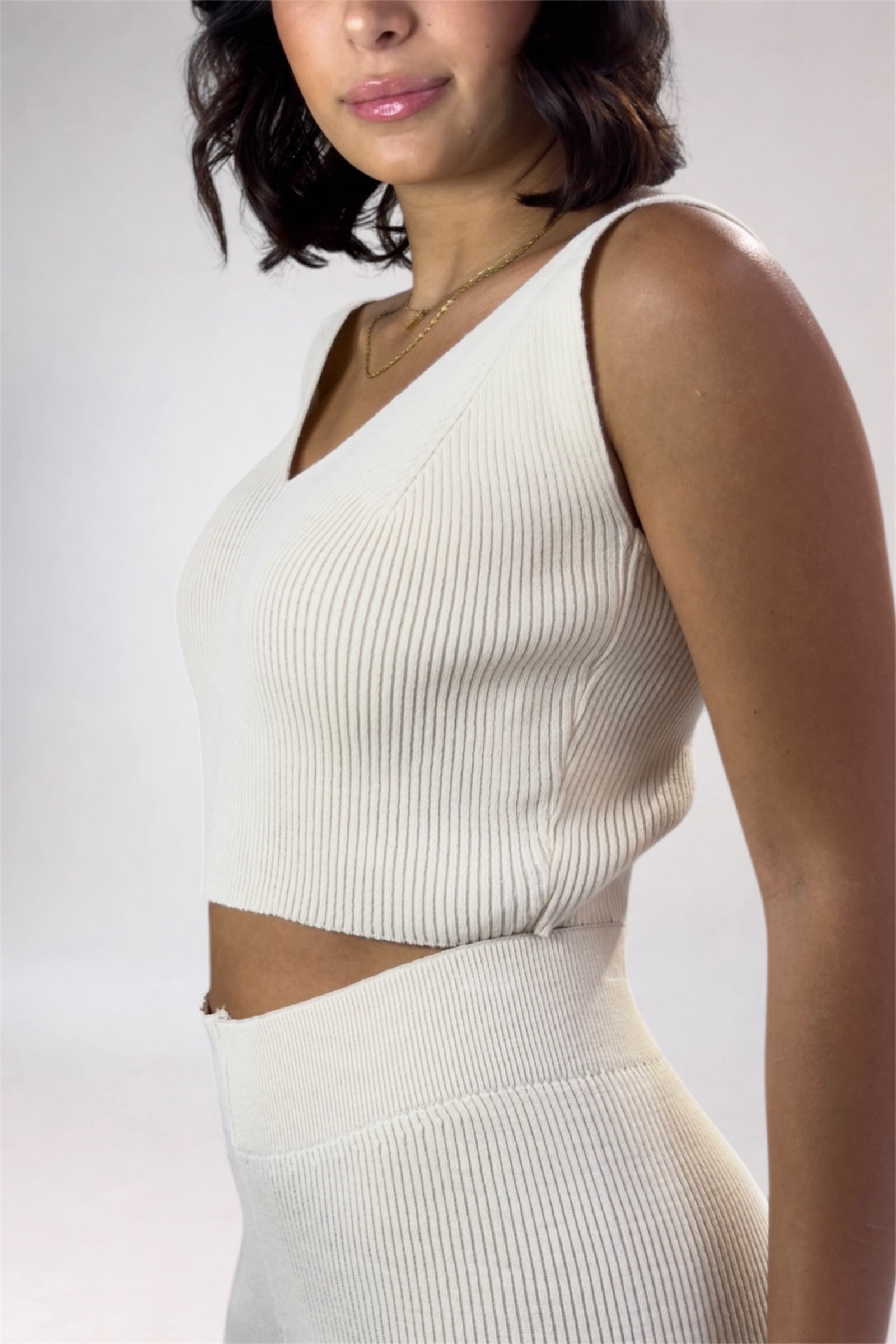 Woman wearing a white ribbed sleeveless top and skirt set against a plain background