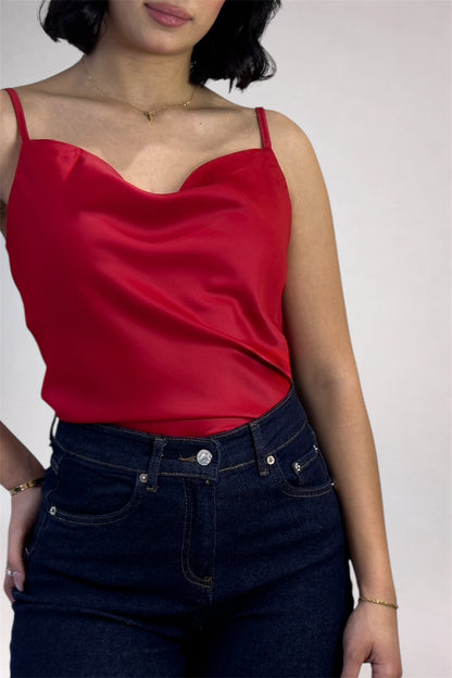 Person wearing a red satin top and dark blue jeans against a plain background