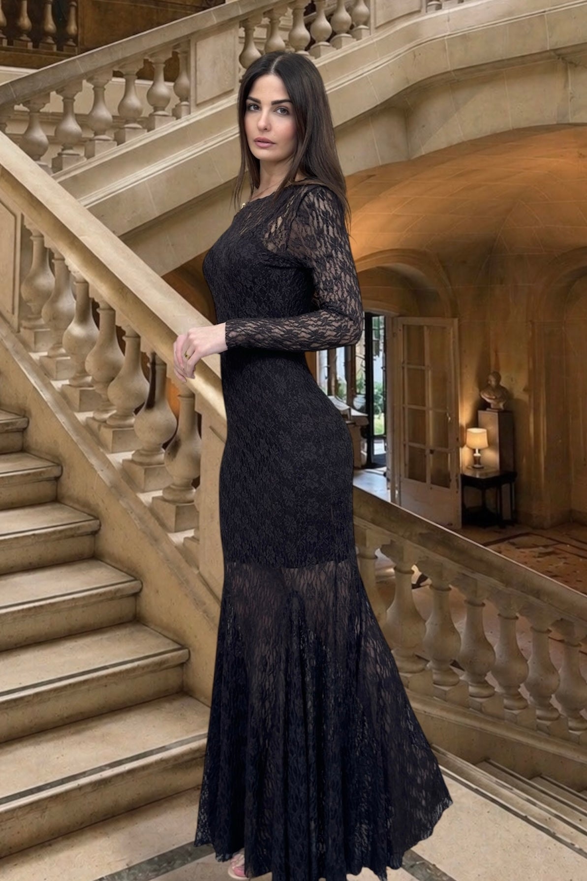 Woman in a black lace dress standing in an elegant interior setting with stairs and decorative elements.