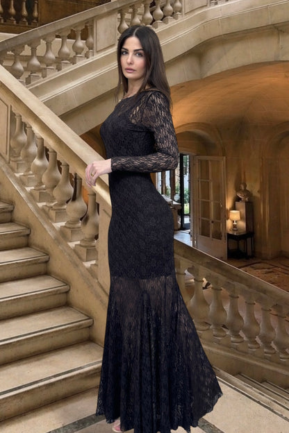 Woman in a black lace dress standing in an elegant interior setting with stairs and decorative elements.