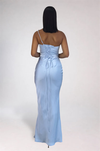 A woman viewed from the back wearing a light blue satin slip dress with a single strap, lace-up back, and tie detail, photographed against a plain light gray studio background.