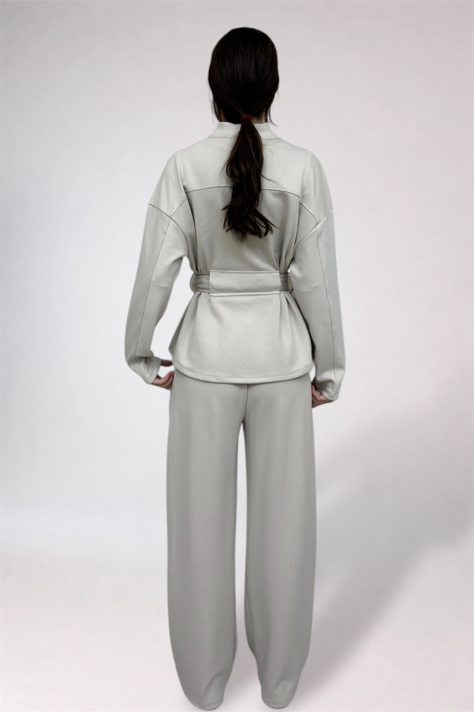Person wearing a light gray outfit with a belt on a white background