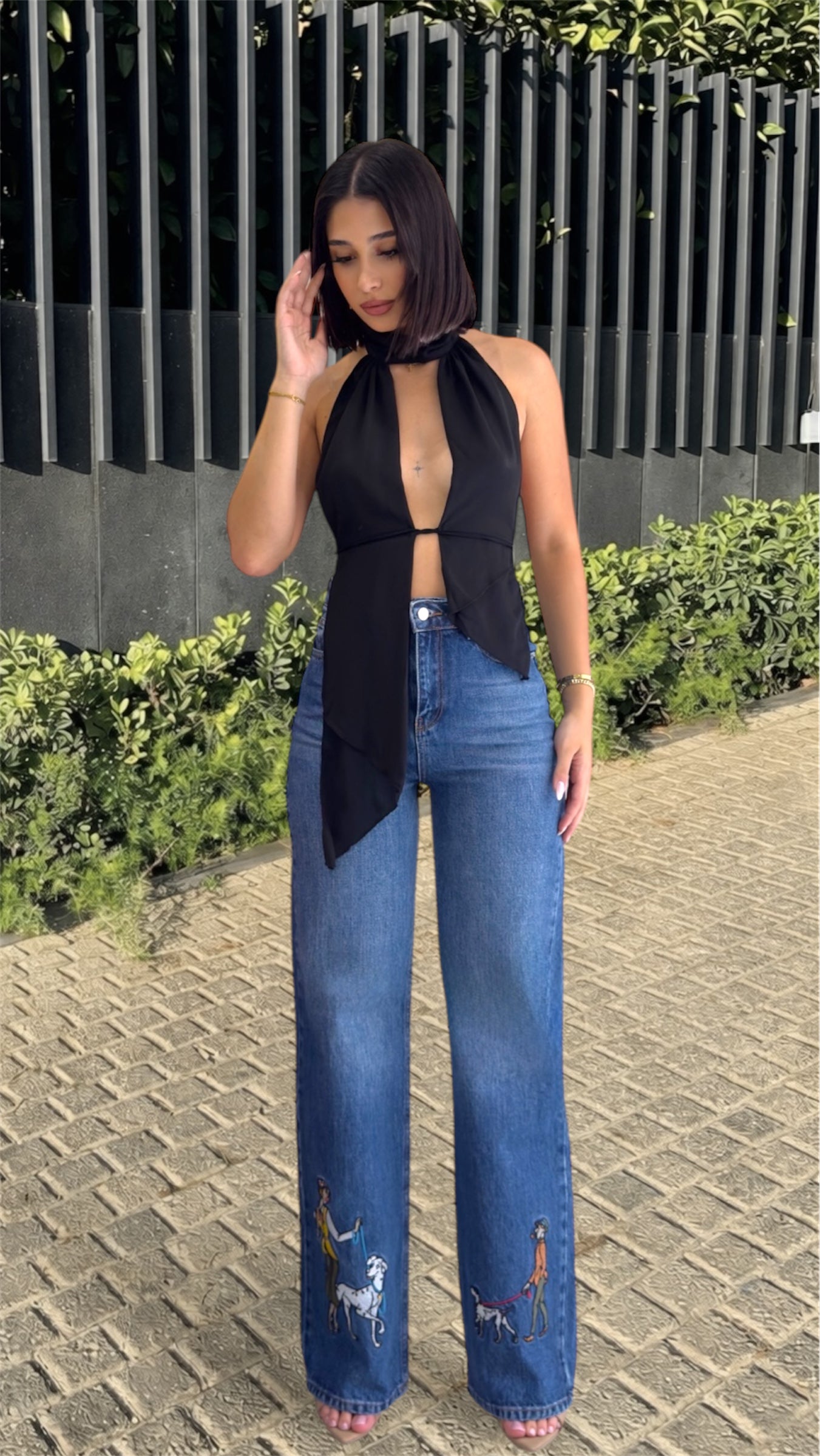 Woman wearing a black top and blue jeans with embroidery outdoors.