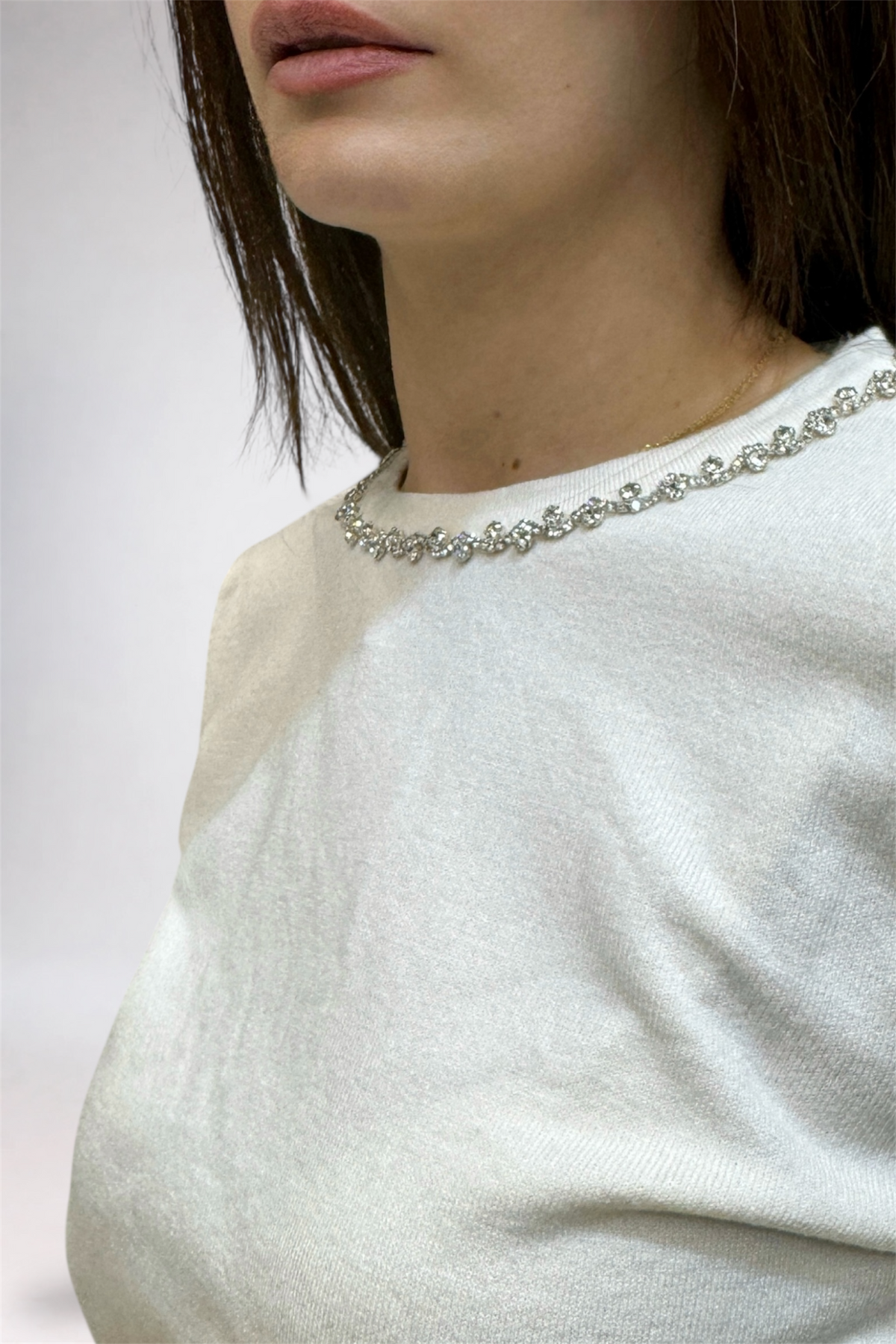 Close-up of a person wearing a white sweater and pearl necklace against a neutral background