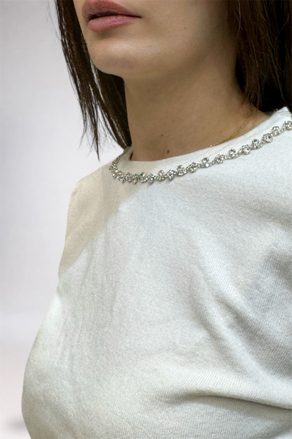 Close-up of a person wearing a white sweater and pearl necklace against a neutral background