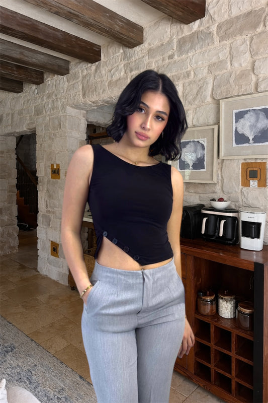 Woman in black top and light blue pants standing in a stone-walled room with wooden beams.