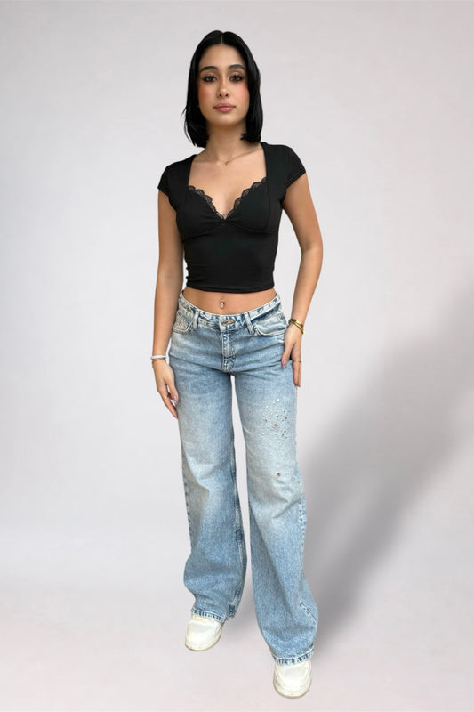Woman wearing a black top and blue jeans on a plain background