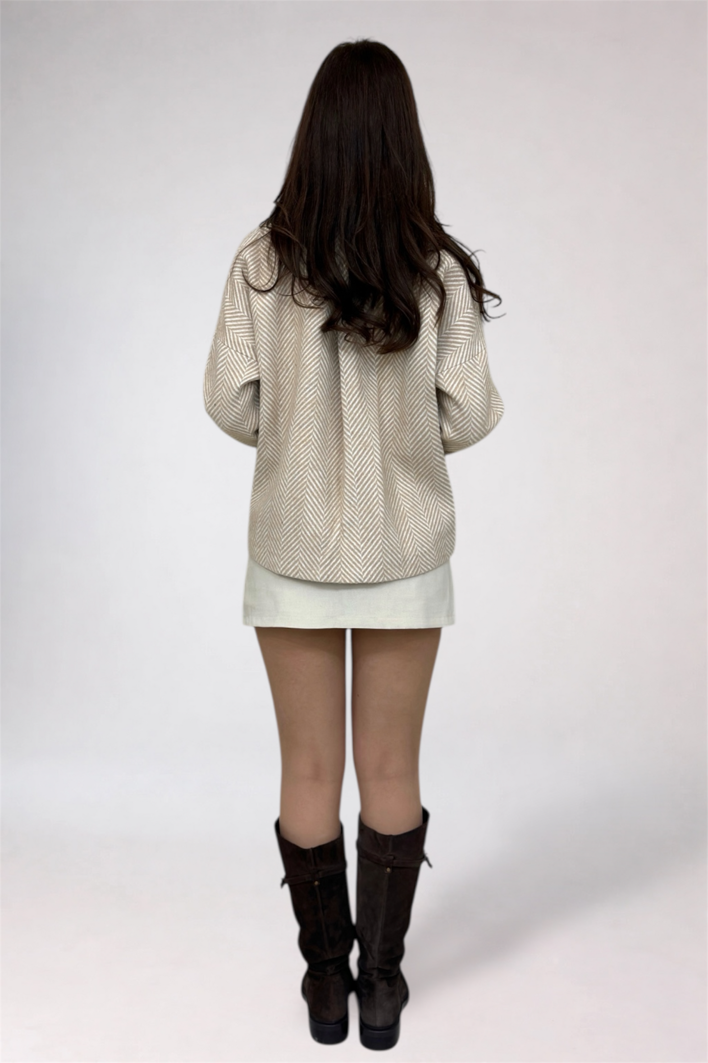 Person wearing a beige textured jacket, white skirt, and black boots on a white background