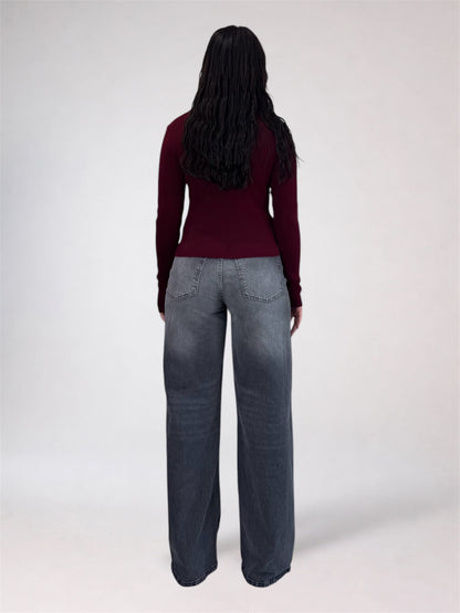 A woman shown from the back wearing a dark burgundy long-sleeve top and wide-leg gray jeans against a plain light gray studio background.