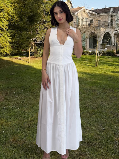 Woman in a white dress standing in a grassy area with trees and a building in the background