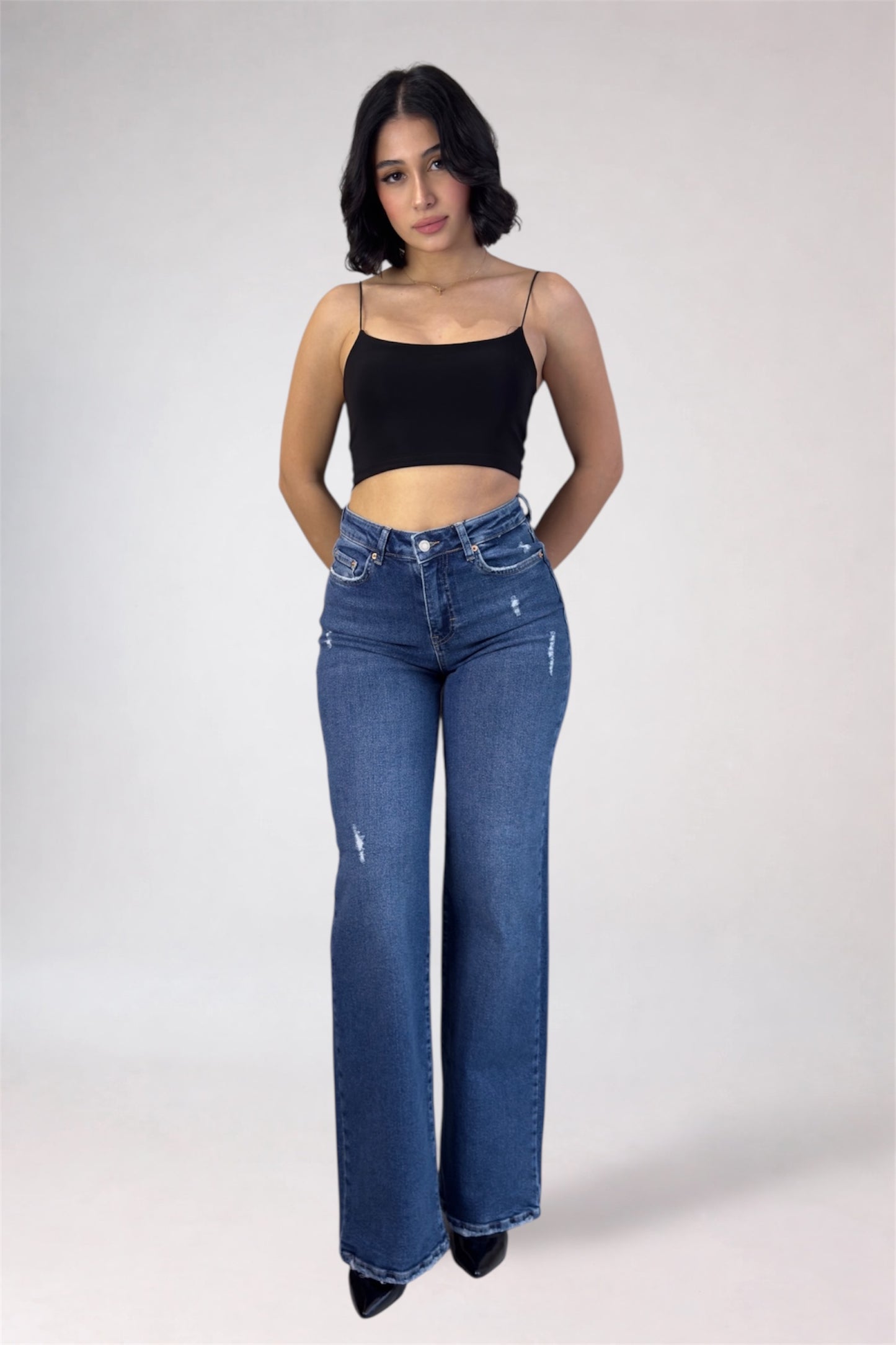 Woman wearing blue jeans and a black top on a white background